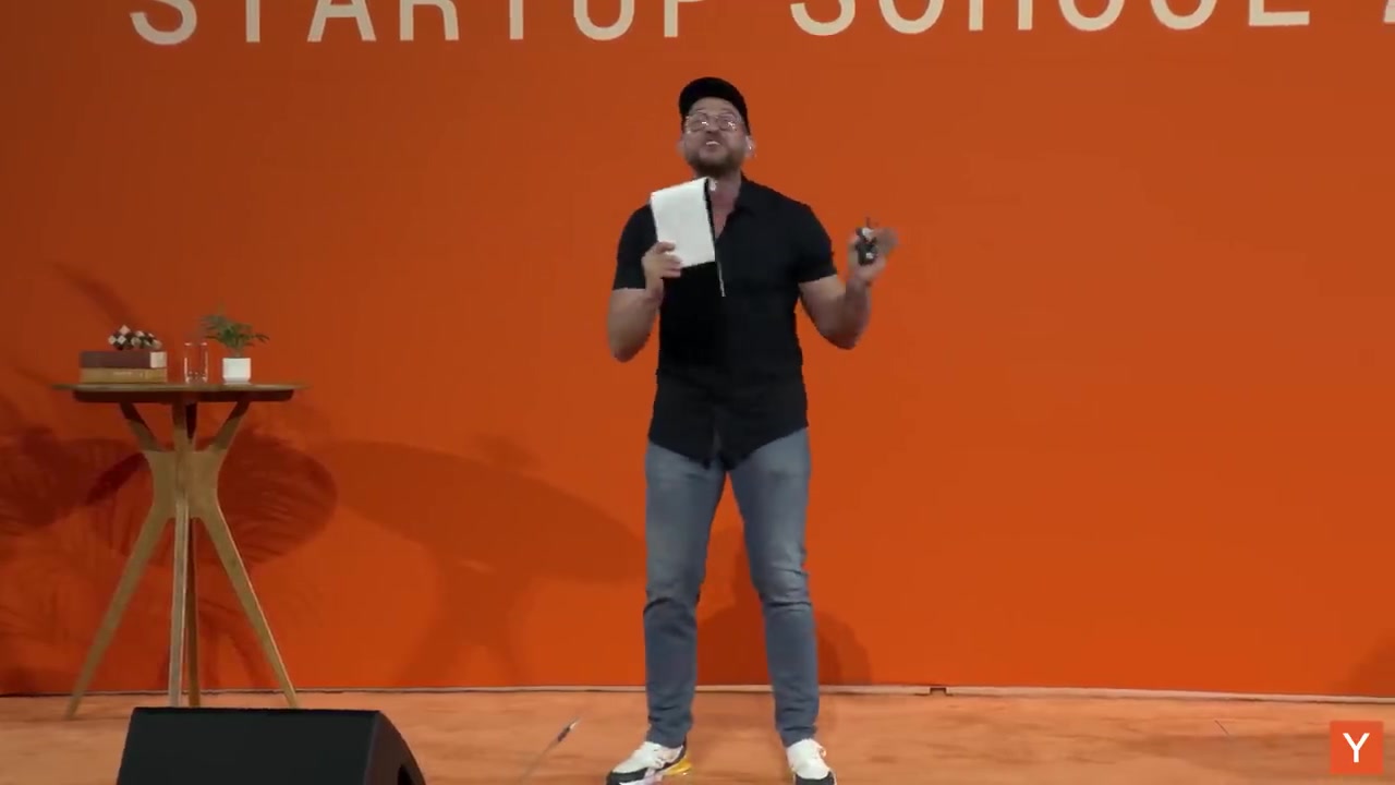 Peter 在橙色舞台上讲话，手持记事本和 clicker